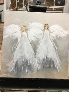 two white angel paintings sitting on top of a easel