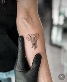 an elephant tattoo on the arm of a woman's left hand, with black gloves