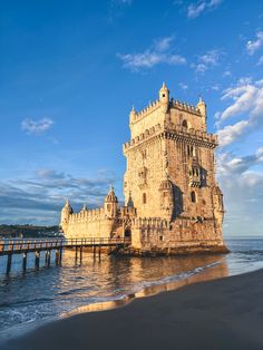 an old castle sitting on top of a beach next to the ocean under a blue sky