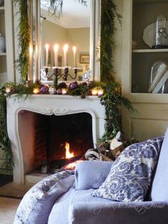 a living room decorated for christmas with candles and greenery on the fireplace mantel