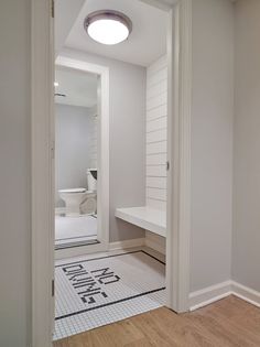 an empty bathroom with white walls and wood flooring is seen through the doorway to another room