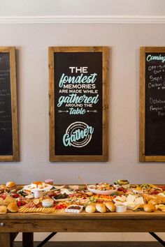 a long table with food on it in front of two chalkboard menus