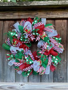 a christmas wreath hanging on the side of a wooden fence with green and red ribbons