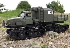 a toy army truck is sitting on the ground next to some rocks and grass with trees in the background