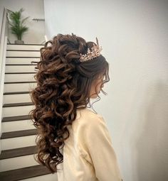 a woman wearing a tiara standing in front of some stairs with long curly hair