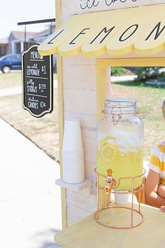 a young boy sitting in front of a lemonade stand