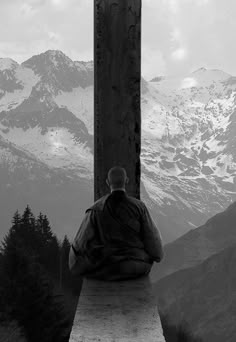 a man sitting on top of a wooden cross in front of snow covered mountain peaks