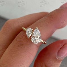 a woman's hand holding a diamond ring with two pear shaped diamonds on it