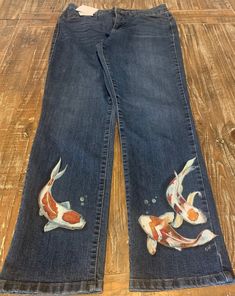 "Beautifully hand painted koi fish in shades of white, red, orange, and yellow on lower part of each leg. Upcycled/recycled Bandolino Jeans - size 12; rise 11\"; inseam 29.5\"; 34\" waist. Hems show no wear; 5 pocket styling. I have been painting for 40 years and have really loved painting on denim. These jeans have been painted with fabric paints/mediums, then heat set. Care instructions will be included with order. (Such as: turn pants inside out, machine wash cold on gentle cycle, etc.) I have several unique items to choose from - take a look. THANK YOU for shopping at FORREST AVENUE STUDIO." Hand Painted Denim Pants, Pant Pocket Design Paint, Painting On White Jeans, Jeans Fabric Painting, Posca On Fabric, Painted Back Pocket Jeans, Hand Painted Jeans Pants, Back Pocket Designs Jeans Painting