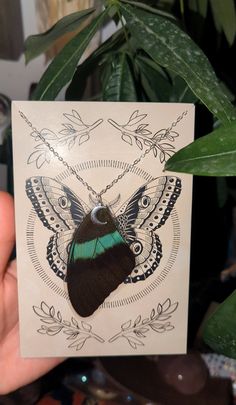 a hand holding up a card with a butterfly on it's back and wings