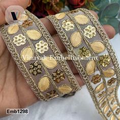 two bracelets with gold flowers and chains on the sides, one is being held by someone's hand