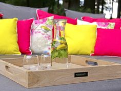 a tray that has some glasses in it on top of a couch with colorful pillows