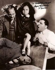 an old black and white photo of three people with one child on his lap, the other sitting down