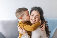 a woman is hugging a young boy on the couch