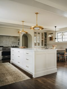 a large kitchen with white cabinets and gold fixtures on the island in front of a dining room table