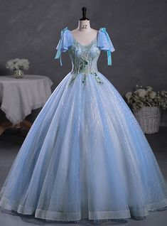 Amidst a sea of elegance, this Quinceanera dress stands out with its breathtaking beauty and charm. The delicate blue hue of the fabric creates a serene and magical aura, perfect for making a grand entrance. The bodice features intricate embroidery in green and silver, adding a touch of nature-inspired sophistication. Adorned with charming blue bows on the shoulders, the dress exudes a playful yet elegant vibe. The full skirt, crafted from layers of shimmering tulle, flows gracefully to the floor, creating a voluminous and ethereal silhouette. Sparkling details woven throughout the fabric catch the light beautifully, ensuring you shine with every movement. This dress is designed for those who wish to combine classic elegance with a modern twist, making it an ideal choice for a Quinceanera Blue Tulle Ball Gown For Quinceanera, Princess Style Blue Evening Dress For Debutante Ball, Blue Tulle Quinceanera Dress For Banquet, Light Blue Tulle Ball Gown For Debutante Ball, Blue Princess Ball Gown With Fitted Bodice, Light Blue Tulle Gown For Quinceanera, Blue Floor-length Quinceanera Dress For Debutante Ball, Blue Floor-length Wedding Dress For Quinceanera, Blue Floor-length Quinceanera Dress