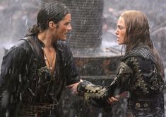 a man and woman standing in the rain holding each other's hands while talking