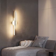 a gray couch sitting next to a wall mounted light on the side of a wall