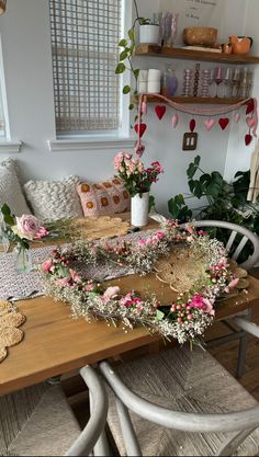 a wooden table topped with lots of flowers and greenery next to a white chair