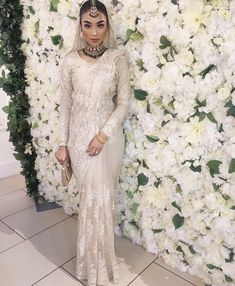 a woman standing in front of a flower wall wearing a white dress and headpiece