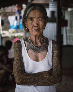 an old woman with tattoos on her arms and chest is standing in front of other people