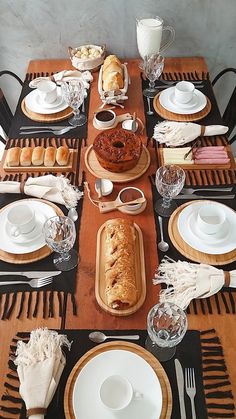 a wooden table topped with lots of white plates and silverware next to a loaf of bread