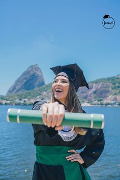 a woman wearing a graduation cap and gown is holding a green stick in front of the water