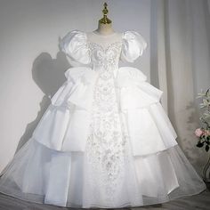 a white wedding dress on a mannequin with flowers in the corner behind it