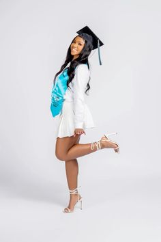 a woman posing for the camera in her graduation cap and white dress with high heels