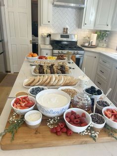 a wooden cutting board topped with bowls filled with fruit and dips next to bread