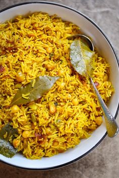 a white bowl filled with yellow rice and vegetables next to a spoon on top of a table