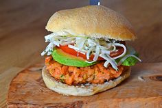 a chicken burger with lettuce and tomato on a wooden cutting board