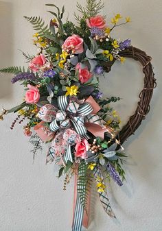 a heart shaped wreath hanging on the wall with flowers and ribbons attached to it's sides