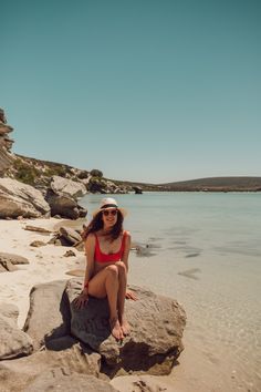 a woman sitting on top of a rock near the ocean