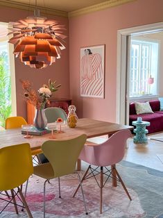 a dining room with pink walls and yellow chairs around the table in front of a purple couch