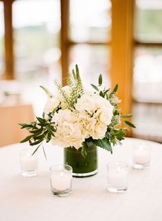 white flowers and greenery in a green vase on a round table with votive candles