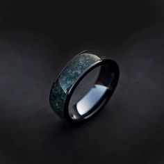 a black ring with green marble inlays on the inside, against a dark background