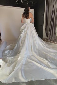 a woman in a white wedding dress is standing near a wall and looking at something