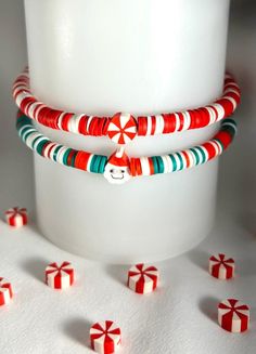 three red and green bracelets sitting on top of a white cup next to candy canes