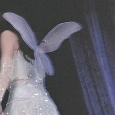 a woman in a white dress with blue fairy wings on her head and hands behind her back