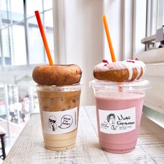 two drinks are sitting next to each other on a table with doughnuts in the background