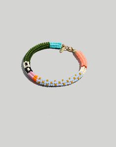 the multicolored bracelet with gold clasp is shown on a gray background and has an orange, yellow, green, pink, and white bead