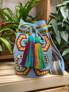 a small blue bag with tassels on the front and side, sitting on a wooden bench