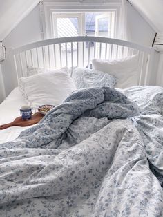 an unmade bed with blue and white comforter in a loft space next to a window