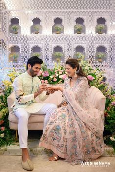 a man and woman sitting next to each other on a couch in front of flowers