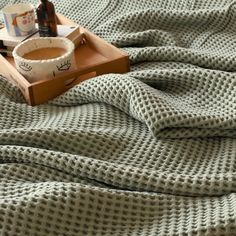 a tray with a cup of coffee sitting on top of a bed next to a blanket