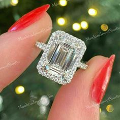 a woman's hand holding an engagement ring with a large emerald stone in the center