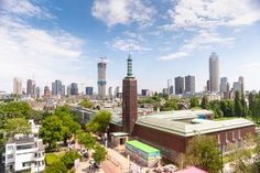 an aerial view of a city with tall buildings and trees in the foreground, on a sunny day