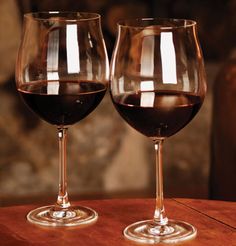 two wine glasses sitting on top of a wooden table next to each other with red wine in them