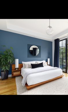 a bedroom with blue walls and white bedding, hardwood flooring, large mirror on the wall